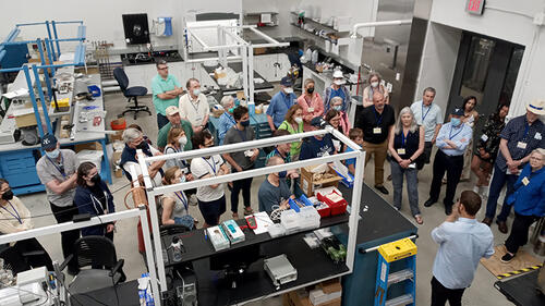 group of people standing in a lab looking at someone speaking.