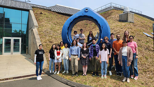 group of people standing in front of a large, circular sculpture