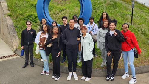 group of people standing in front of a large, blue circular sculpture and posing.