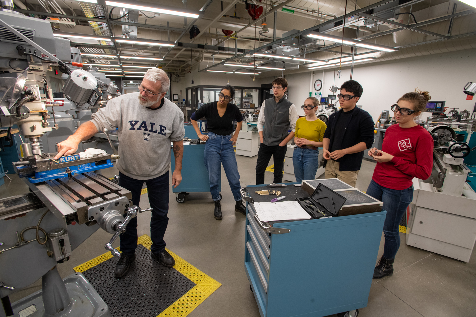 Instructor in machine shop pointing out how to use milling machine to group of students who are watching.