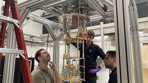 3 people with structures around them, including a dilution fridge insides.