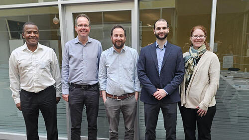 5 people standing in a row, smiling.