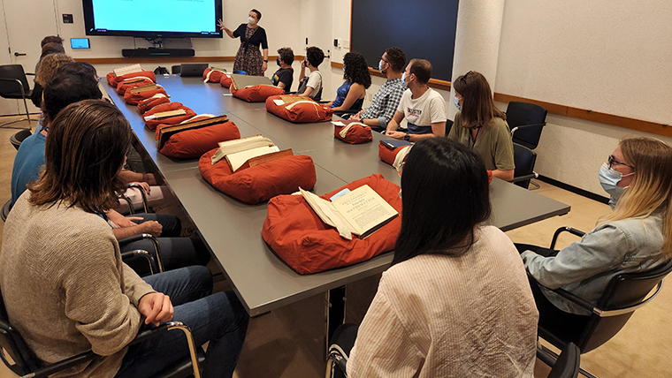 people sitting at a table with books on pillows in front of them watching an instructor at a screen.