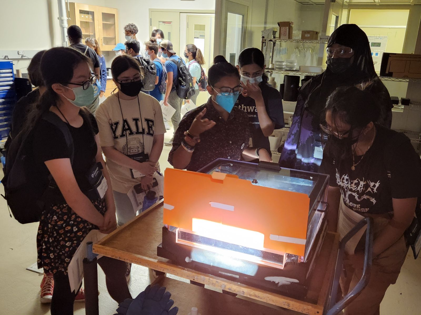 a group of people standing around a table with a cloud chamber on it.
