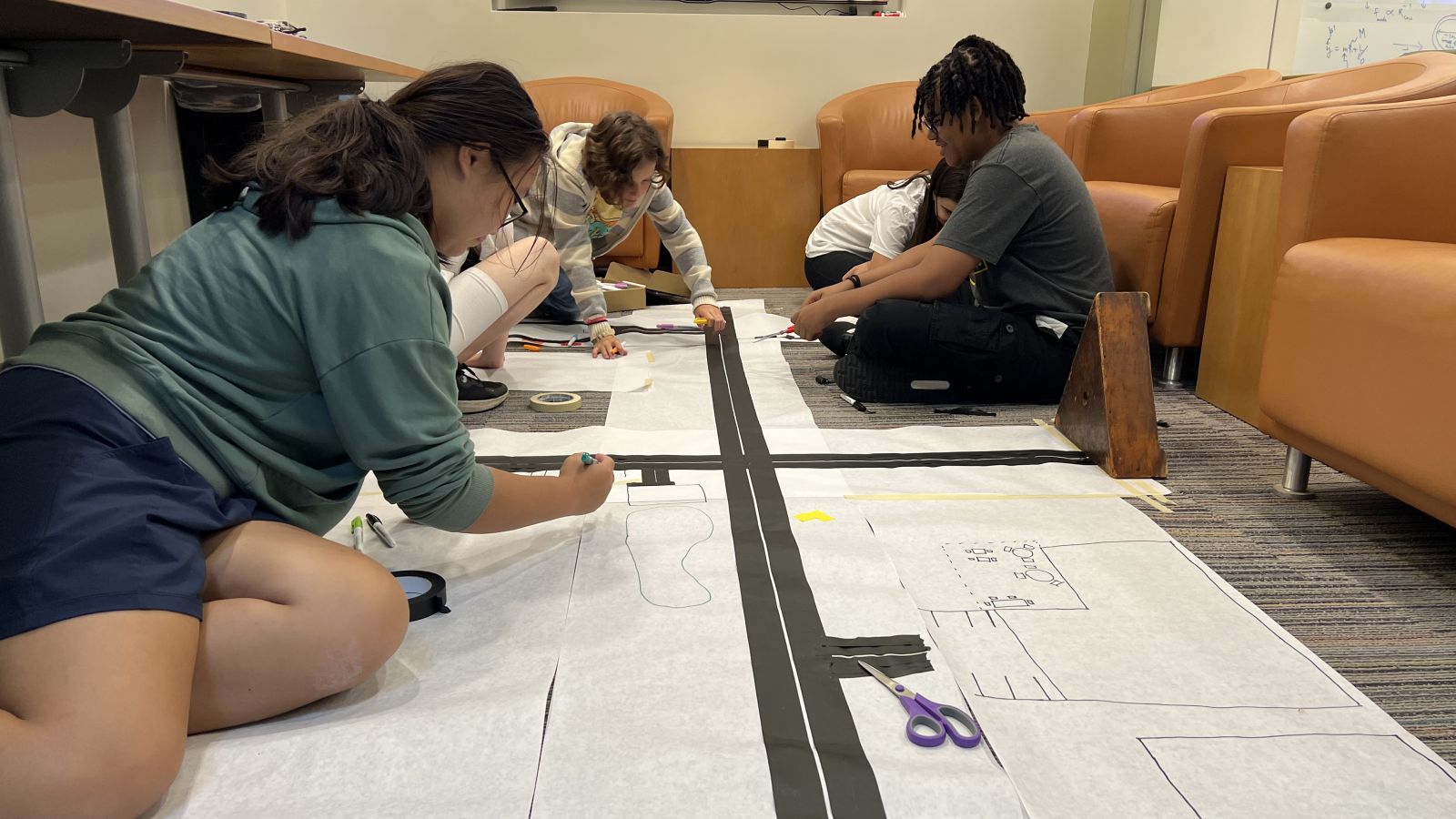 students sitting on floor drawing on large pieces of paper.