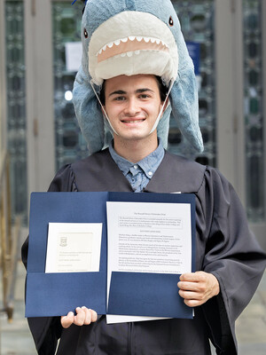 headshot of a person wearing a stuffed shark on his head as a hat and holding a blue folder with documents in it.