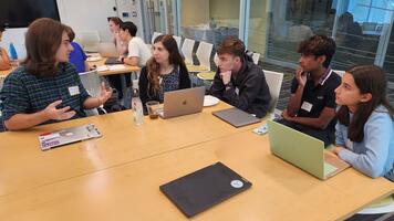 a small group of people gathered at a table with laptops in front of them talking.