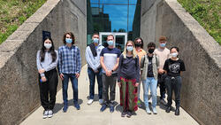 9 people posing in front of a building with masks on.