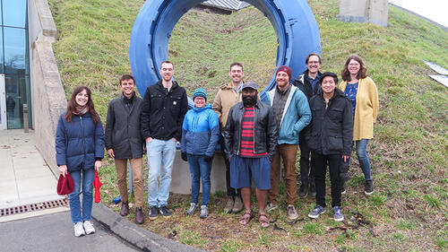 10 people standing in front of a large blue circular sculpture and smiling.