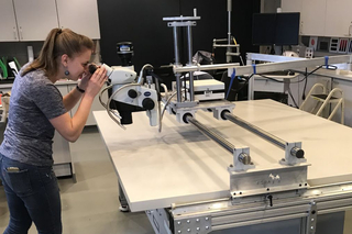 Person looking through microscope mounted on bridge built with Wright Lab APC collaboration.