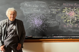 John Harris in front of a blackboard covered in diagrams.