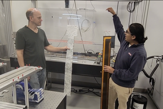 two people in a clean room with ATLAS detector parts.