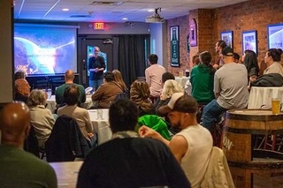 Group of people sitting at tables listening to a speaker at the Pint of Science Festival.