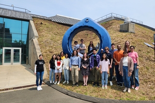 2023 Summer Students posing outside Wright Lab in front of blue, circular Portal sculpture.