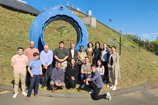HAYSTAC collaboration members posing in front of large, blue circular sculpture outside of Wright Lab.