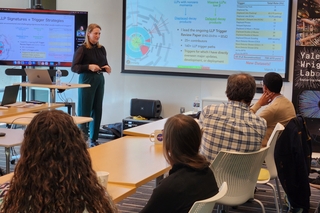 Kiley Kennedy giving a NPA seminar standing in front of a screen with data on it; audience members at table facing speaker.