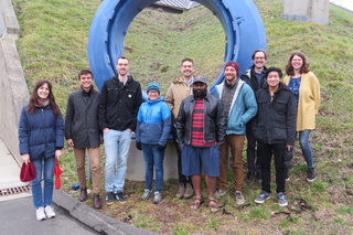 Simons Observatory members posing in front of large, blue, circular sculpture outside of Wright Lab.