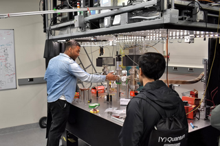 YQI fellow Cedric Wilson during a tour of Charles Brown's lab showing tabletop experiment to a person.