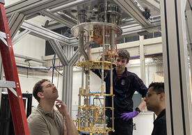 3 people with structures around them, including a dilution fridge insides.