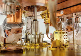 two people in clean room garb working on a large detector.