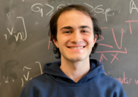 headshot of person wearing a Yale hoodie in front of chalkboard with writing on it.