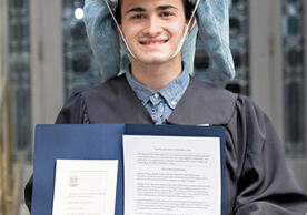 headshot of a person wearing a stuffed shark on his head as a hat and holding a blue folder with documents in it.