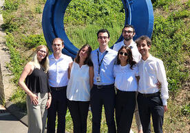7 people standing in front of a large blue circular sculpture in front of a building.