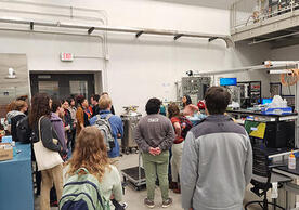 group of people standing in a lab space listening to a speaker.