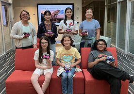 7 people posing holding robots and smiling.