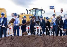 group of people with shovels in dirt wearing hardhats.