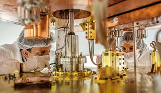 Two people in clean room gear building CUORE detector cryostat instrumentation.