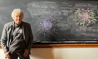 John Harris in front of a blackboard covered in diagrams.