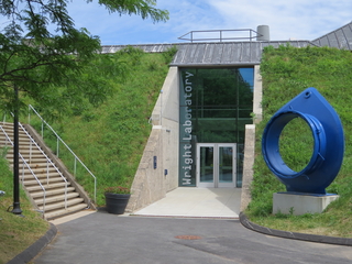 building entrance with stairs on left, blue circular sculpture on right. entrance built into a hill.