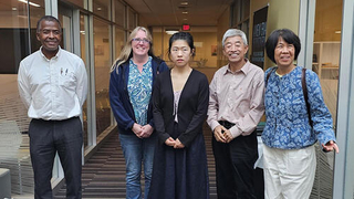 Pan in middle with four other people standing near by facing camera.