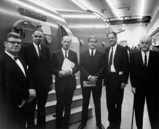6 dignitaries standing in front of an accelerator tank.