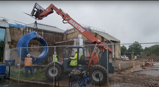 construction equipment lifting large blue circular sculpture in front of Wright Lab.