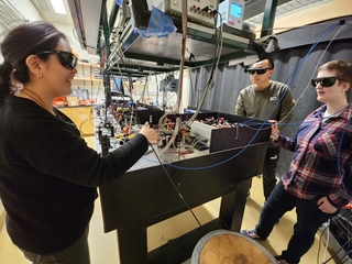 Faculty member Reina Maruyama mentoring two graduate students at an optical table.