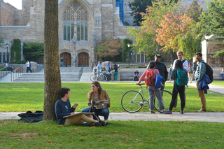 People hanging out in front of Yale University Library. Two people in front of tree, 3 walking with bike.