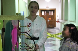 Josie Rose in Ghostbuster Costume showing demo in Sloane Phyiscs Lab hallway to a student.