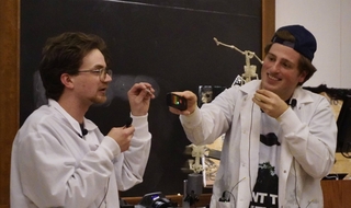 Greg Penn and Andrew Tamis doing physics demo in lab coats at Sloane Physics Laboratory.