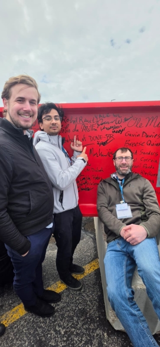 Three people posing in front of a signed red beam.