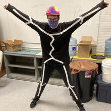 Person standing with arms outstretched and legs spread with black costume on with white lines on it.