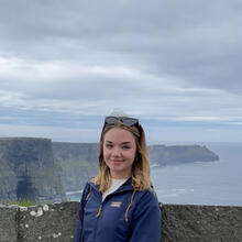 Person standing in front of Irish scenery.