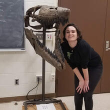 person standing in room by mounted dinosaur skull.