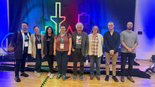 8 Wright Lab Relativistic Heavy Ion group members standing in front of Quark Matter 2025 logo.