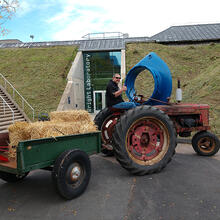 person sitting on tractor with cart of hay in front of building.