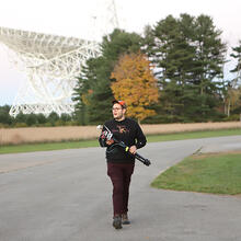 person standing in front of a radio telescope holding equipment.