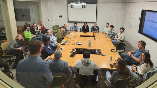 people sitting in a room around a group of tables.