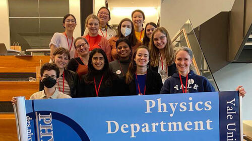 group of people standing behind a sign smiling.